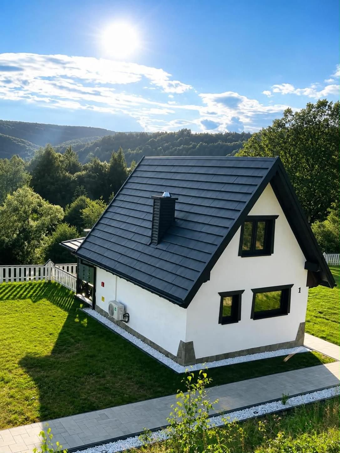 Biały dom Kalina Farm House z ciemnym dachem na zielonym zboczu, w tle zalesione wzgórza w słońcu