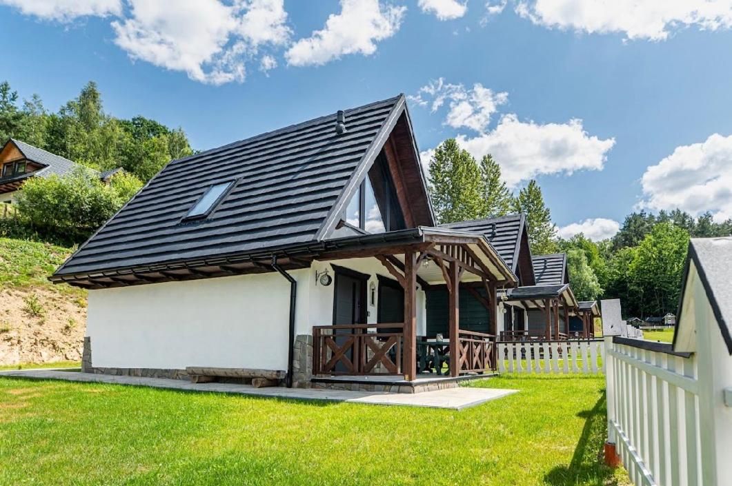 Biały dom z ciemnym dachem i drewnianym tarasem na tle nieba